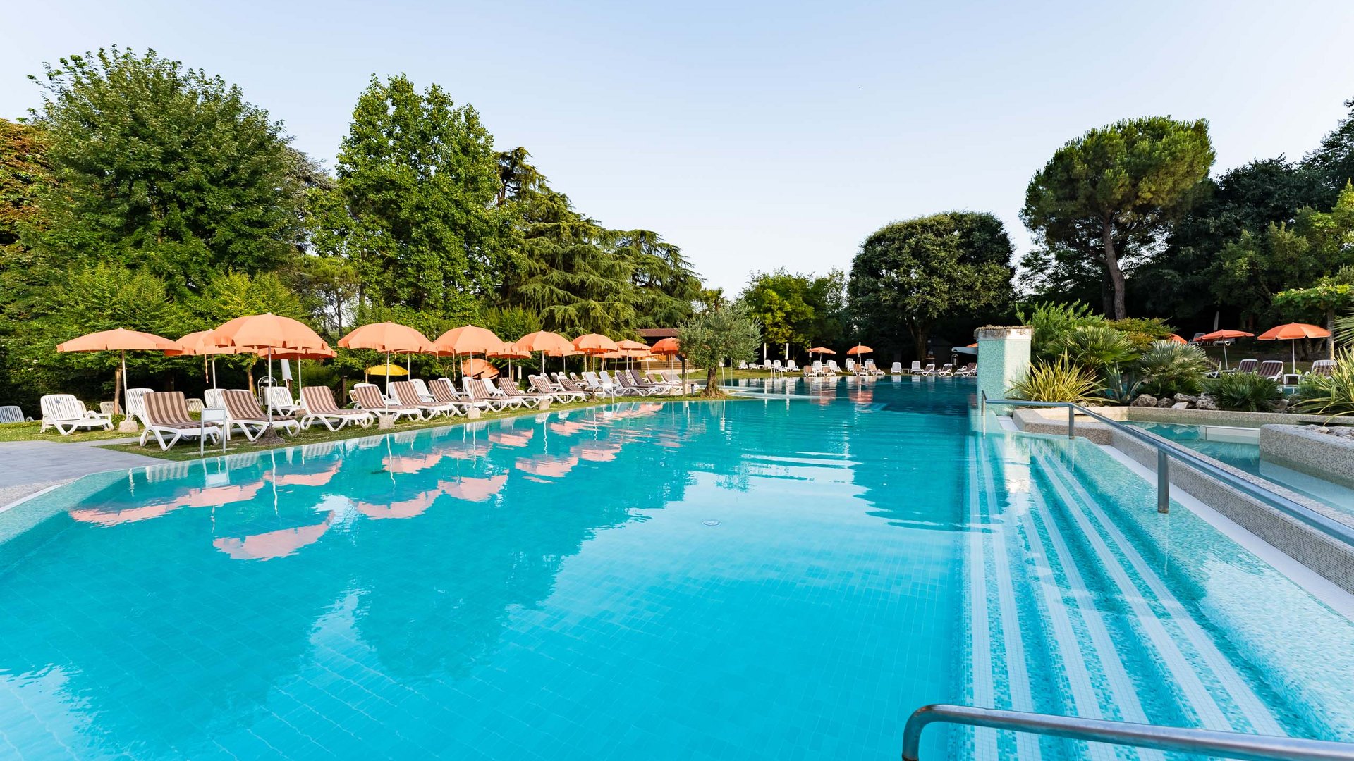 Piscina all'aperto con ombrelloni arancioni e lettini vicino al verde